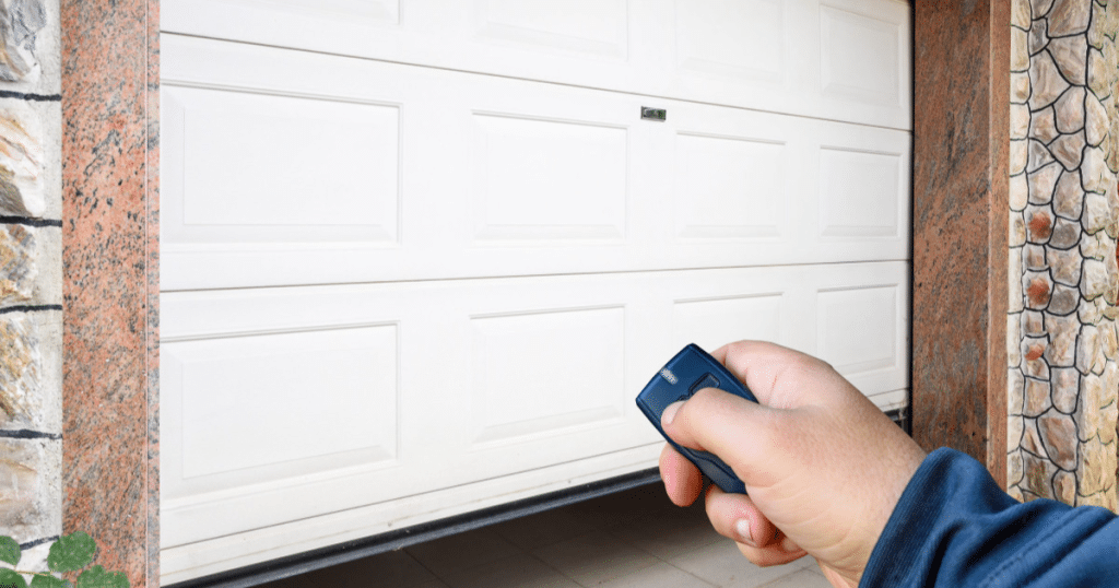 Hand using a remote to open a white garage door.